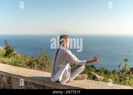 Profilo di una donna che fa yoga in cima a una scogliera in montagna. Donna medita nello yoga asana Padmasana. Foto Stock