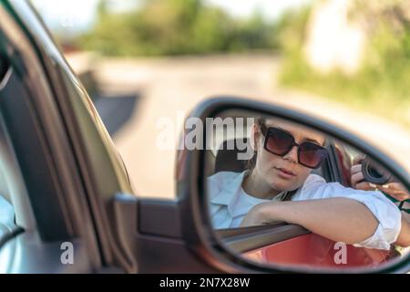 Donna auto specchio. Ritratto di una bella donna in una nuova auto guardando nello specchio retrovisore. Foto Stock