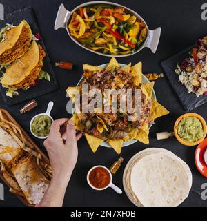 mano del prodotto che prende i nachos dalla piastra Foto Stock