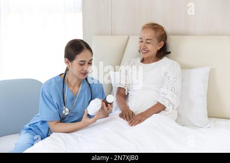 Infermiere cura paziente anziano donna asiatica anziana presente uso di droga per i pazienti recupero a letto a casa Foto Stock