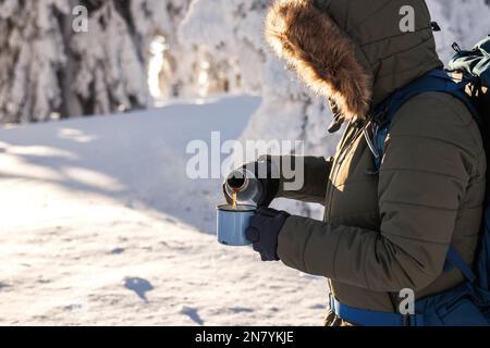 Escursionista che versa la bevanda calda dai thermos nella tazza da viaggio. Rinfresco durante il trekking invernale nelle giornate fredde Foto Stock