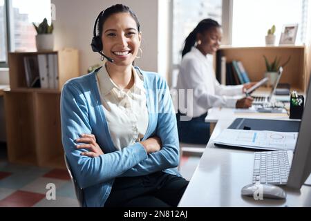 Il personale è felice di fare affari. un giovane uomo d'affari che utilizza un auricolare e un computer in un ufficio moderno con la sua collega che lavora in background. Foto Stock