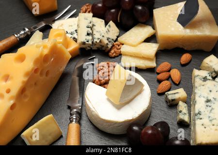 Composizione con diversi tipi di formaggio e coltelli su tavola nera, primo piano Foto Stock