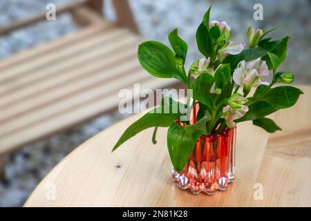 Un piccolo bouquet di fiori si trova in un vaso di vetro su un tavolo di legno. Alstroemeria, comunemente chiamata il giglio peruviano o giglio degli Inca Foto Stock