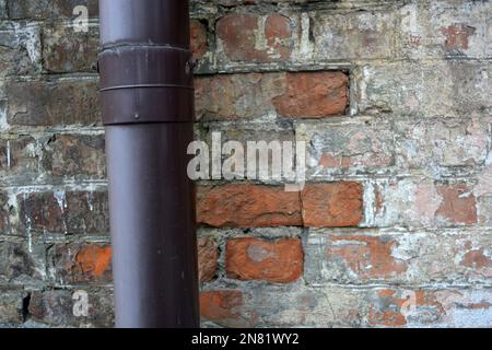 Una vecchia parete rossa di scabby con un grande tubo viola di plastica e un tubo giallo sottile. Foto Stock