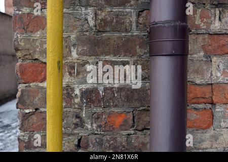 Una vecchia parete rossa di scabby con un grande tubo viola di plastica e un tubo giallo sottile. Foto Stock