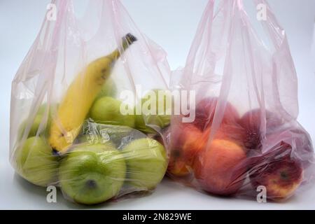 Due grandi confezioni di frutta, cibo sano, molte mele rosse, mature e mele verdi con una banana matura si trovano in sacchetti rosa monouso. Foto Stock