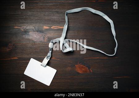 Badge vuoto con cordino su sfondo in legno. Scheda id in plastica vuota. Badge in plastica bianca. Giacitura piatta. Foto Stock