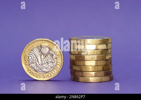 Monete della Sterlina Britannica una si è levata in piedi sul bordo e otto impilate sul lato destro Foto Stock