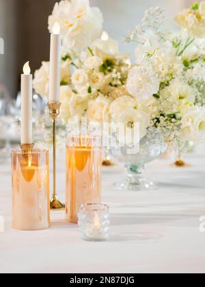 Tavolo servito per banchetti. Candele elettriche e vere in portacandele lucido come decorazione. Tavolo con tovaglia bianca e composizione floreale. Bouquet Foto Stock