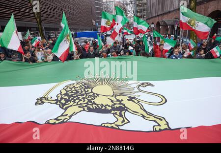 Amburgo, Germania. 11th Feb, 2023. I partecipanti a una manifestazione contro il regime iraniano detengono una bandiera iraniana di grandi dimensioni sulla via Lange Mühren. L'Unione iraniana aveva chiesto la manifestazione. Sotto lo slogan "sostegno e solidarietà al popolo iraniano - protesta contro il regime iraniano”, i partecipanti si sono trasferiti da Mönckebergstraße al Rathausmarkt. Credit: Georg Wendt/dpa/Alamy Live News Foto Stock