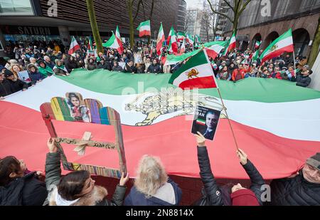 Amburgo, Germania. 11th Feb, 2023. I partecipanti a una manifestazione contro il regime iraniano detengono una bandiera iraniana di grandi dimensioni sulla via Lange Mühren. L'Unione iraniana aveva chiesto la manifestazione. Sotto lo slogan "sostegno e solidarietà al popolo iraniano - protesta contro il regime iraniano”, i partecipanti si sono trasferiti da Mönckebergstraße al Rathausmarkt. Credit: Georg Wendt/dpa/Alamy Live News Foto Stock