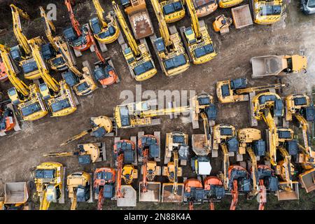 Vista aerea direttamente sopra un cantiere di noleggio di macchinari industriali pesanti con scavatori e bulldozer parcheggiati insieme in un contesto industriale Foto Stock