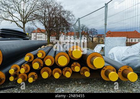 Riscaldamento isolato nero tubi grandi con tappi di plastica gialli giacciono su un cantiere. Alberi ed edifici residenziali sullo sfondo Foto Stock