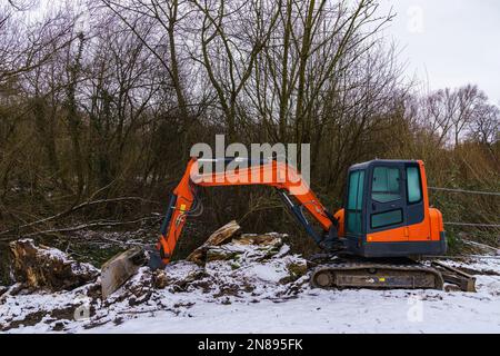 Un piccolo escavatore che rastrellava il terreno in un cantiere innevato. Foto Stock