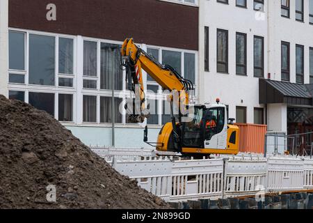 Escavatore giallo in un cantiere di costruzione contro un edificio bianco. Foto Stock