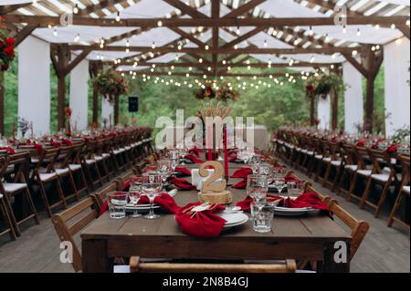 Un grande, lungo, decorato, tavolo e sedie in legno, con piatti, fiori, candele. Padiglione nella foresta in natura. Banchetto di nozze. banchetto in natura Foto Stock