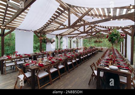 Un grande, lungo, decorato, tavolo e sedie in legno, con piatti, fiori, candele. Padiglione nella foresta in natura. Banchetto di nozze. banchetto in natura Foto Stock