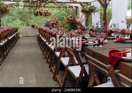 Un grande, lungo, decorato, tavolo e sedie in legno, con piatti, fiori, candele. Padiglione nella foresta in natura. Banchetto di nozze. banchetto in natura Foto Stock