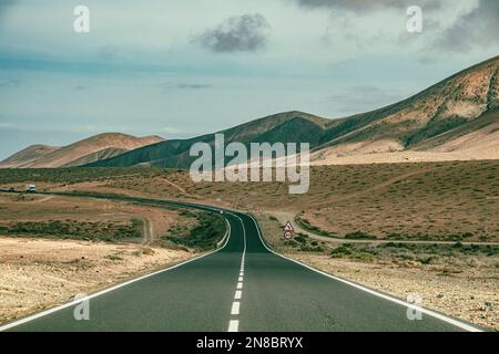 Affascinante strada cinematografica in Spagna con veicolo in lontananza con il deserto su entrambi i lati e bello cielo blu nuvoloso perfetto viaggio estivo caldo weathe Foto Stock