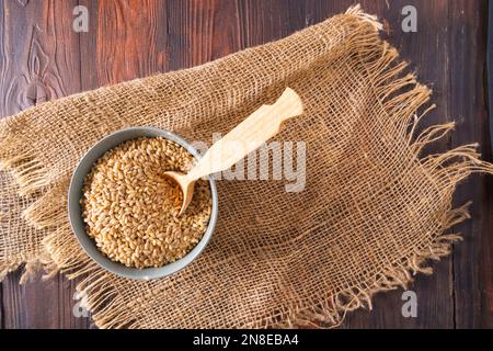 Orzo di perla crudo secco in ciotole e cucchiaio su sfondo di legno, vista dall'alto, piatto. Foto Stock