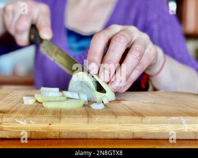 Primo piano di una donna che taglia la cipolla su un asse di legno Foto Stock