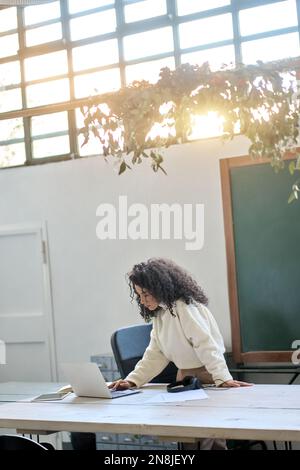 Una giovane donna insegnante o una lavoratrice che si trova alla scrivania e utilizza un computer portatile in ufficio. Foto Stock