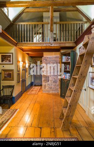 Corridoio con ampie pavimentazioni in legno di pino, scale di Miller, libreria e soppalco al piano superiore all'interno della vecchia casa risalente al 1805. Foto Stock