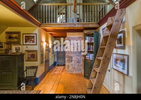 Corridoio con ampie pavimentazioni in legno di pino, scale di Miller, libreria e soppalco al piano superiore all'interno della vecchia casa risalente al 1805. Foto Stock