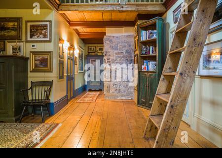 Corridoio con ampie pavimentazioni in legno di pino, scale di Miller, libreria e soppalco al piano superiore all'interno della vecchia casa risalente al 1805. Foto Stock