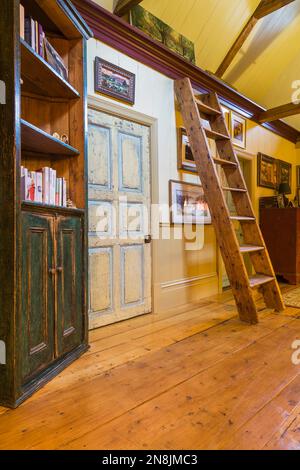 Corridoio con ampie pavimentazioni in legno di pino, libreria, scale di Miller e porte della camera da letto in difficoltà al piano superiore all'interno della vecchia casa risalente al 1805. Foto Stock