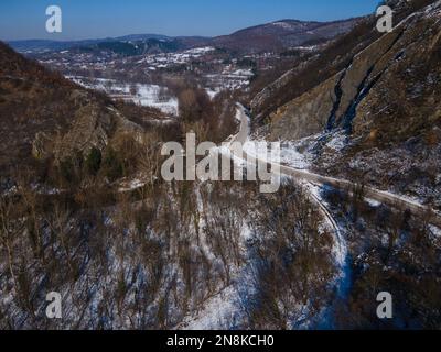 Vista aerea del drone sulla strada che attraversa la collina e la montagna in inverno giorno coperto di neve con rocce e alberi Foto Stock