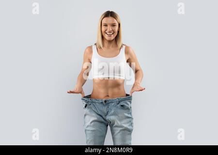 Donna bionda allegra che indossa pantaloni grandi e sorridente Foto Stock