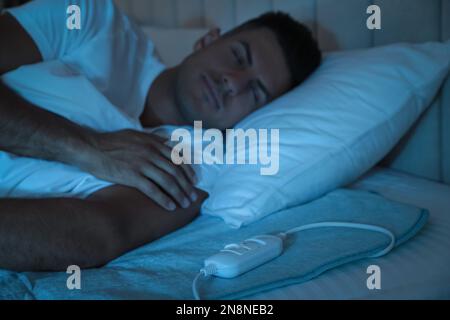 Uomo che dorme sul cuscino riscaldante elettrico a letto di notte Foto Stock