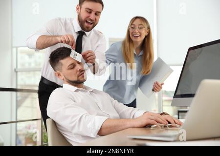 I colleghi prendono nota con la parola Fool al volto del collega in ufficio. Scherzo divertente Foto Stock