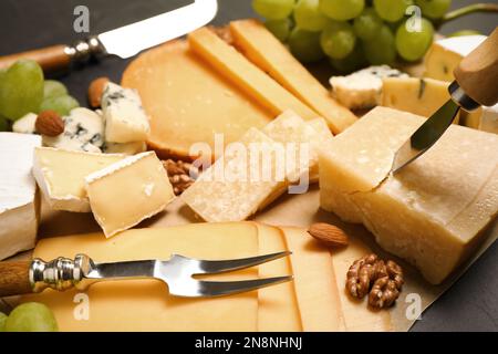 Composizione con diversi tipi di formaggio e coltelli su pergamena, primo piano Foto Stock