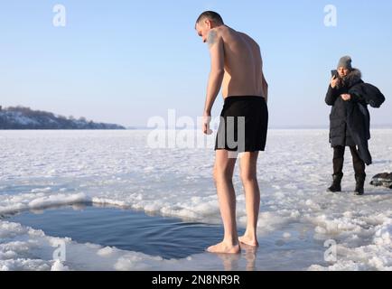 MYKOLAIV, UCRAINA - 06 GENNAIO 2021: Uomo in piedi vicino alla buca di ghiaccio il giorno d'inverno Foto Stock