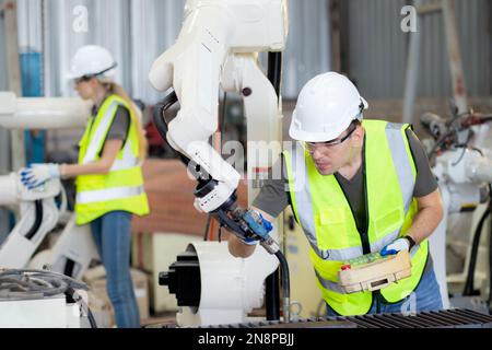 Giovane ingegnere caucasico uomo che utilizza il telecomando con ai robot macchina braccio automatico per la produzione in fabbrica, robotica elettronica AN Foto Stock