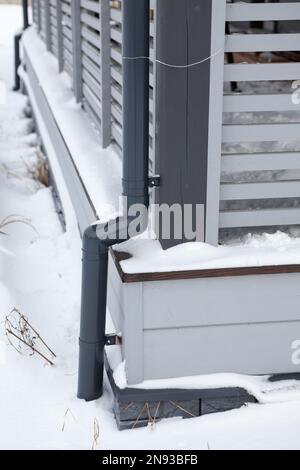 Sistema di downpipe con acqua piovana per veranda in legno di casetta, congelata e coperta di neve Foto Stock