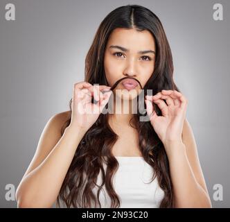 Non disordine con la ragazza disordinata dei capelli. Studio ritratto di una giovane donna attraente facendo un baffi con i suoi capelli su uno sfondo grigio. Foto Stock