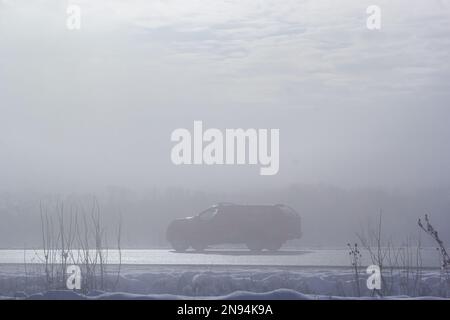 Auto passeggeri nella nebbia su una strada invernale con grandi nevicate sul lato della strada. Foto Stock