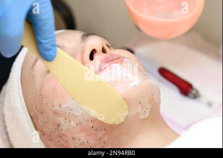 Il processo di applicazione di una maschera idratante al viso in un salone termale, applicando la maschera con una spatola. Foto Stock