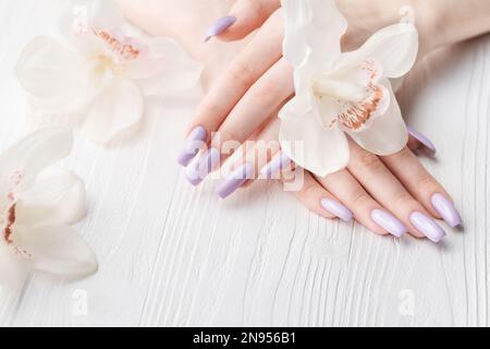 Mani di ragazza con delicata manicure viola e fiori di orchidea. Il concetto di bellezza e cura del corpo. Foto Stock