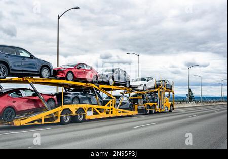 Carro di trasporto per auto di grandi dimensioni professionale di livello industriale trattore semi-autocarro giallo che trasporta le auto sul semirimorchio idraulico modulare in marcia Foto Stock