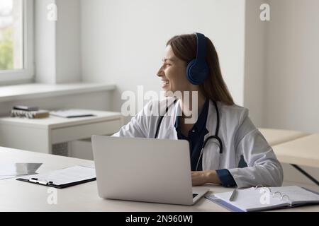 Allegro sogno grazioso medico in cuffie che lavorano al computer portatile Foto Stock