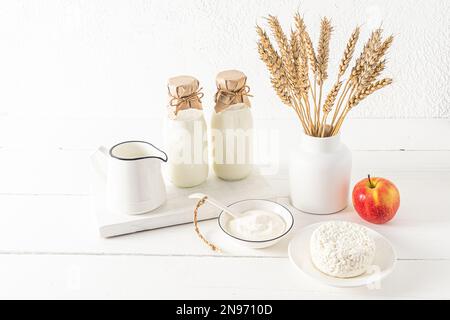 Bella composizione festiva per la vacanza ebraica di Shavuot. latticini su un asse di legno bianco e un vaso con orecchie da pane. sfondo bianco Foto Stock