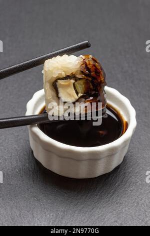 I Chopsticks tengono il sushi su una ciotola di salsa di soia. Primo piano. Sfondo nero Foto Stock