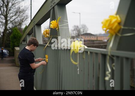 NOTA PER I REDATTORI: IL PERMESSO PARENTALE DATO Ad Un giovane ragazzo lega un nastro giallo con un messaggio di speranza scritto su di esso, ad un ponte sul fiume Wyre in St Michael su Wyre, Lancashire, mentre la polizia continua la loro ricerca per la donna mancante Nicola Bulley, 45, Che è stato visto l'ultima volta la mattina di venerdì 27 gennaio, quando è stata avvistata camminando il suo cane su un sentiero vicino al fiume Wyre. Data immagine: Domenica 12 febbraio 2023. Foto Stock