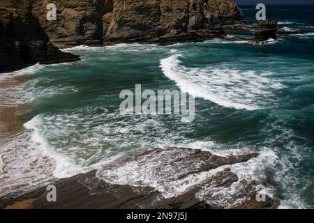 Acqua verde, una colonna di mare e una spiaggia sabbiosa: Ondate atlantiche ondeggianti si estendono per scorrere su lastre stratificate lungo l'aspro Cabo Carvoeiro a Peniche nel distretto di Leiria, Portogallo centrale. Il promontorio combina paesaggi selvaggi con un'abbondanza di fauna selvatica. Foto Stock