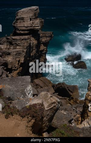 Un'onda di rottura invia il surf Atlantico in alto nell'aria sotto una roccia stratificata stack o pilastro del mare, uno dei molti scolpiti in forme curiose dalle onde e dal vento sparsi lungo la costa frastagliata di Cabo Carvoeiro a Peniche nel distretto di Leiria, Portogallo centrale. Gran parte della roccia sedimentaria fu posata nell'epoca del primo Giurassico, fino a 200 milioni di anni fa. Foto Stock